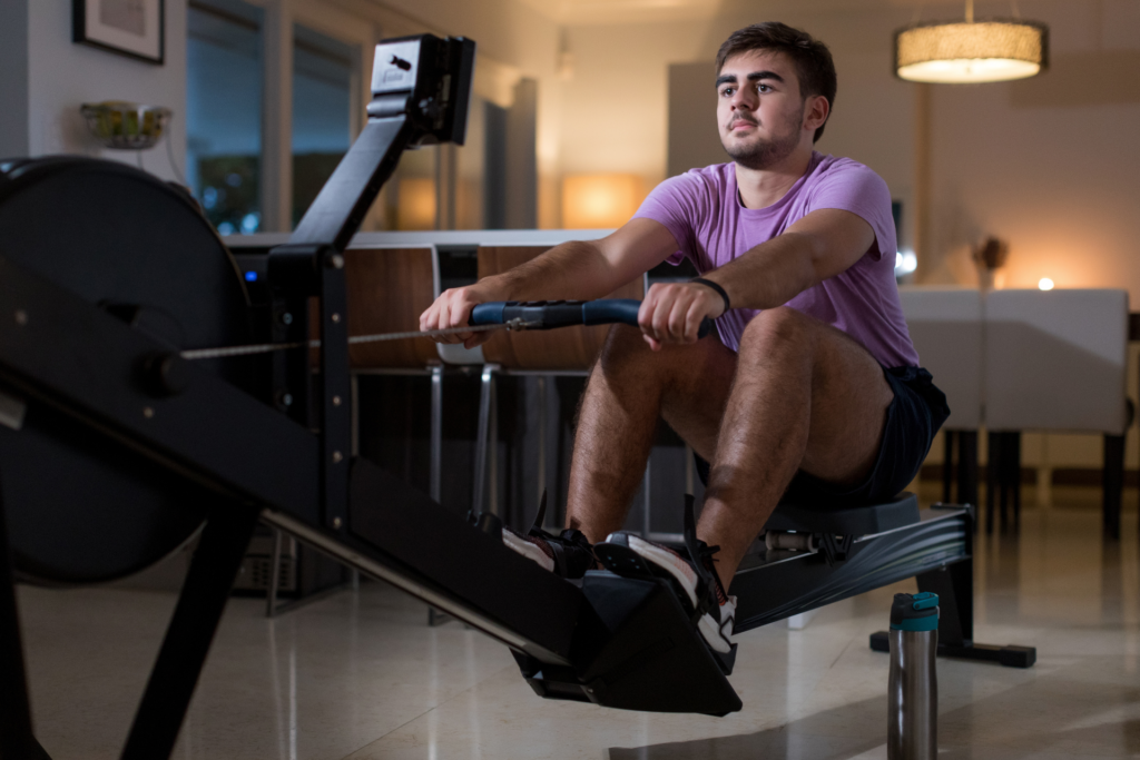 Los 7 Ejercicios Cardiovasculares Más Efectivos Para Quemar Grasa Un hombre entrenando en casa en una máquina de remo